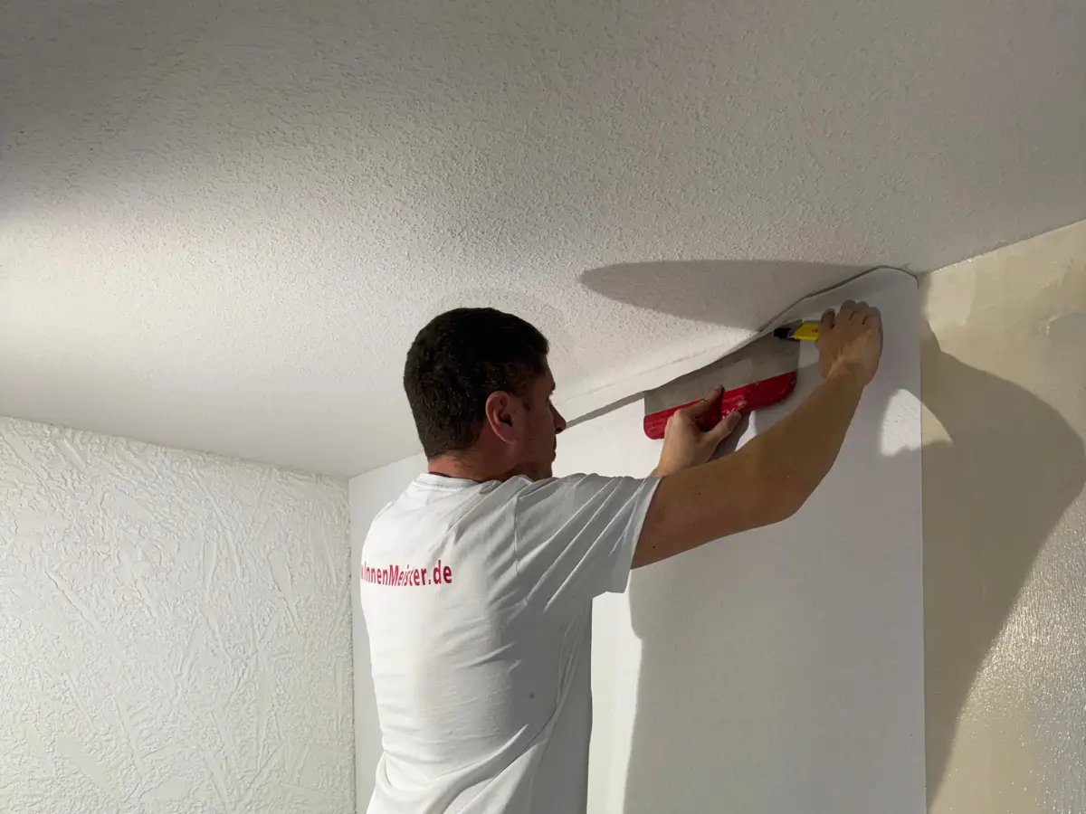Handwerker klebt Raufasertapete an die Wand
